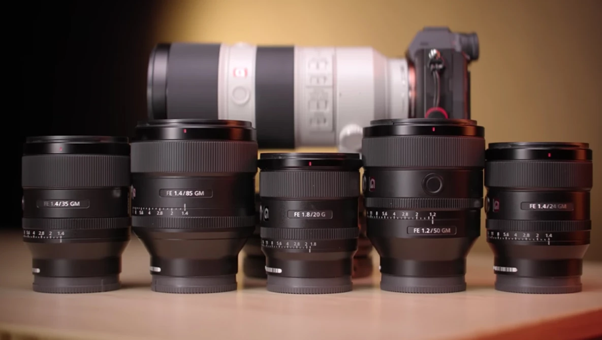 Collection of five prime lenses arranged in front of a telephoto zoom lens and camera body against warm studio lighting.