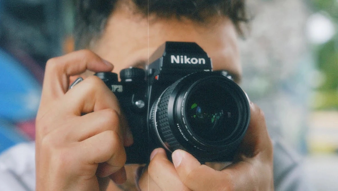 Photographer holding a Nikon DSLR camera up to their face to compose a shot.