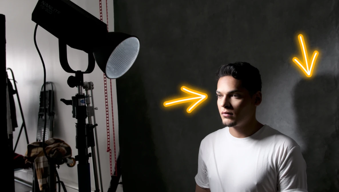 Man in white t-shirt positioned in front of professional studio lighting setup with yellow neon arrows.