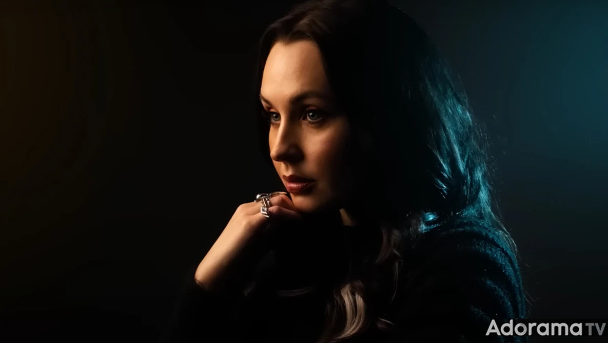 Woman with long dark hair in dramatic low-key studio lighting, gazing downward with contemplative expression.