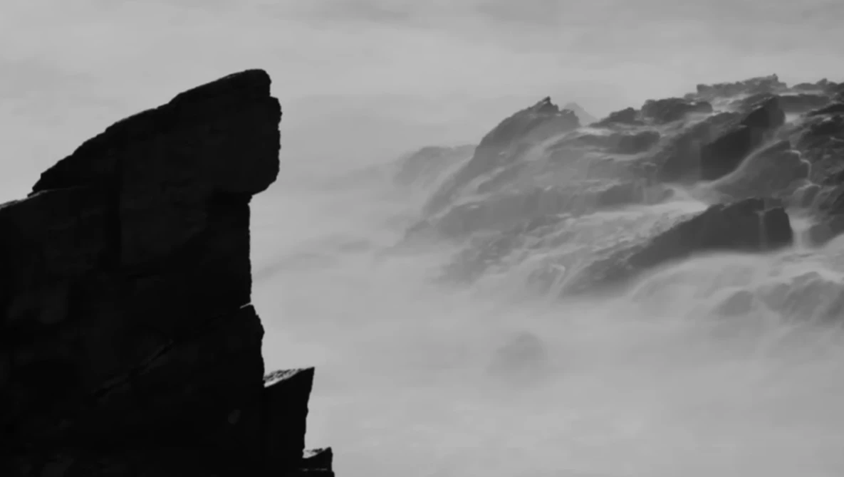 Silhouetted rock formation in the foreground with misty mountains receding into fog and clouds.