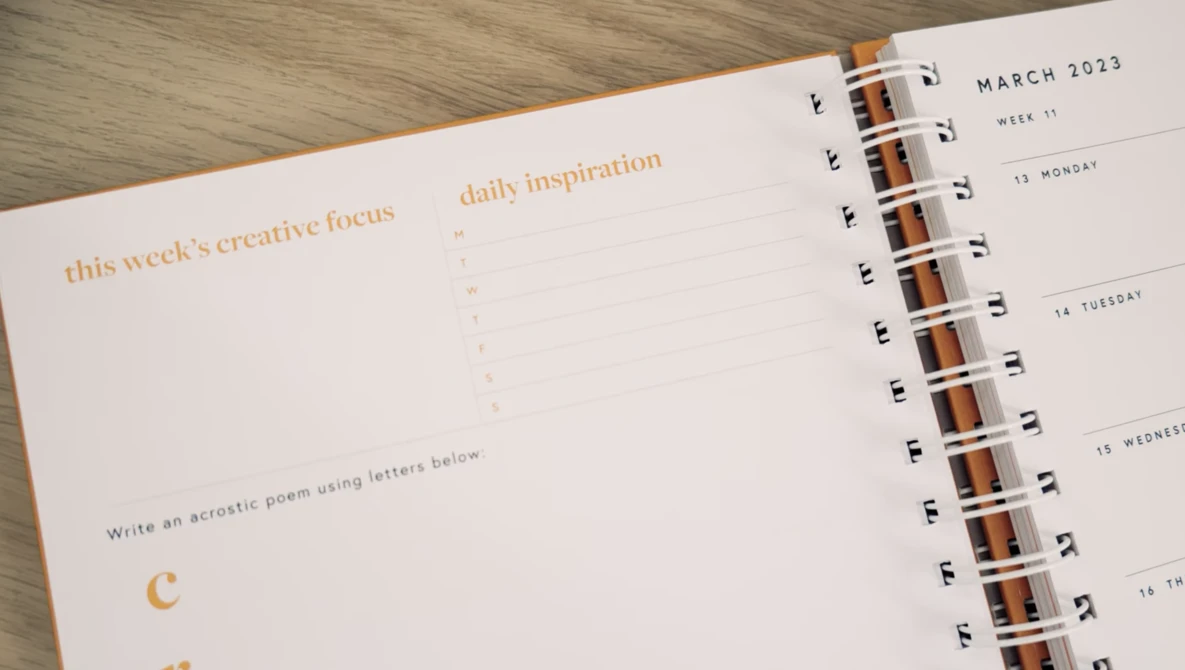 Open spiral-bound planner showing March 2023 week layout with creative writing prompts and daily inspiration sections.