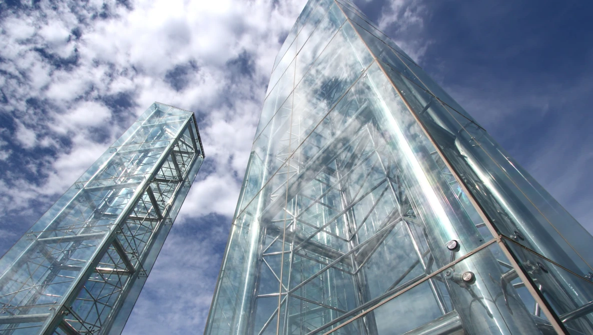 Low-angle view of two steel lattice towers against a bright blue sky with white clouds.