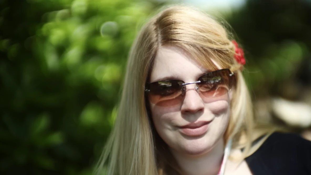 Young woman wearing oversized sunglasses and dark clothing outdoors in natural daylight.
