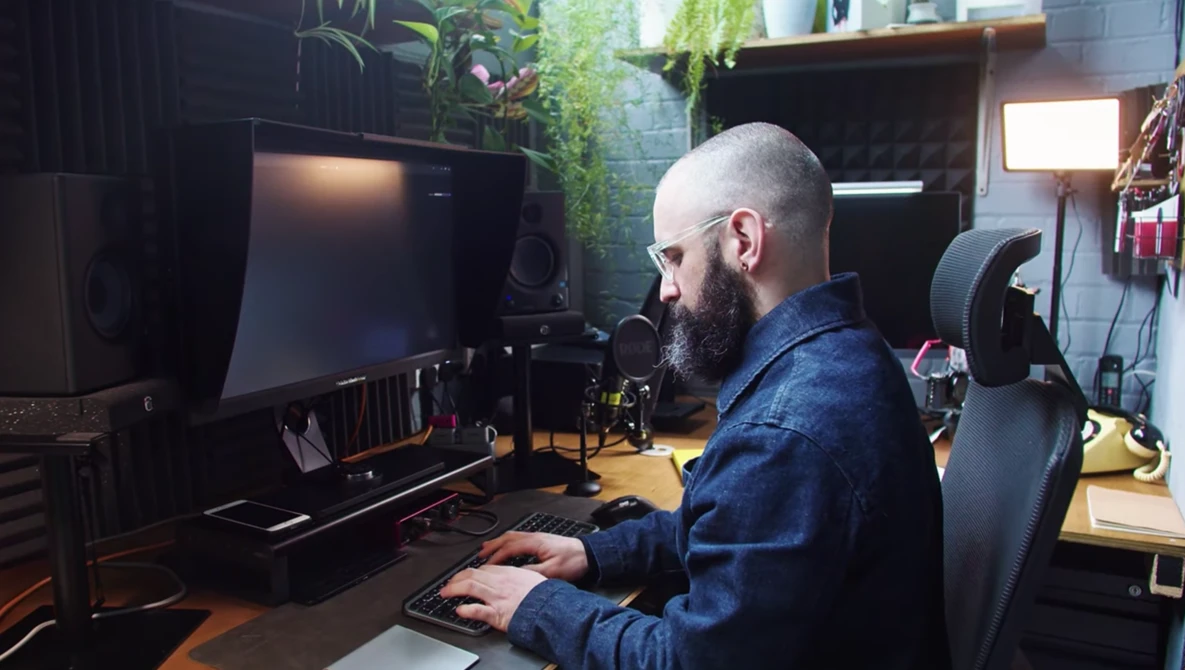 Bearded man working at a computer setup in a creative studio workspace.