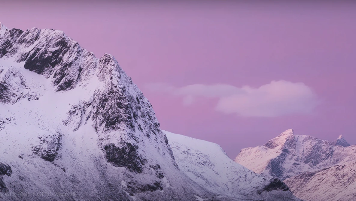 Snow-covered mountain peaks under a dramatic purple and pink sky at dusk or dawn.