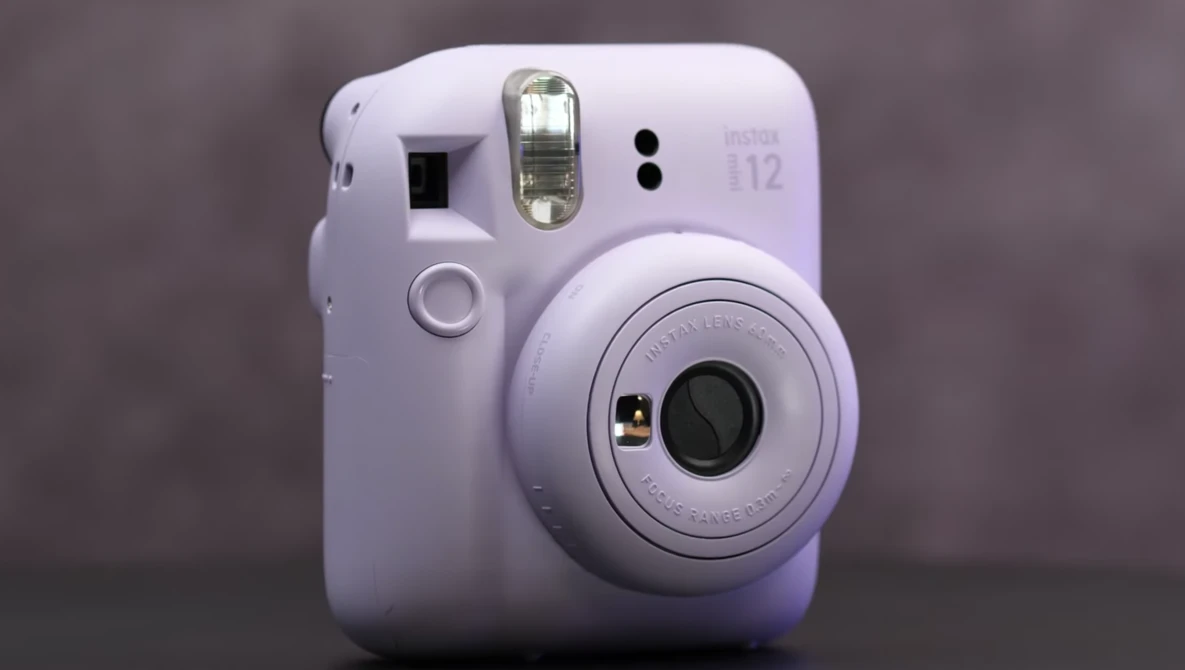 White Fujifilm Instax Mini 12 instant camera with flash and lens visible against neutral background.