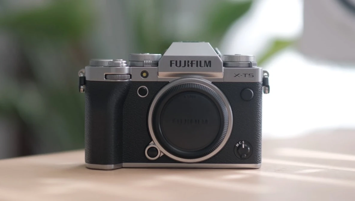 Fujifilm X-T5 mirrorless camera body displayed front-on against a blurred outdoor background.