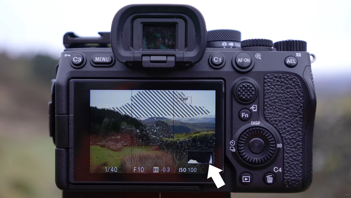 Mirrorless camera displaying live view of a rural building with metal roof and surrounding landscape on its rear LCD screen.