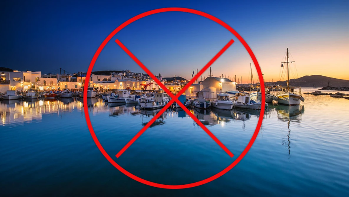 Red prohibition symbol overlaid on a Mediterranean harbor at twilight with boats and illuminated waterfront buildings.