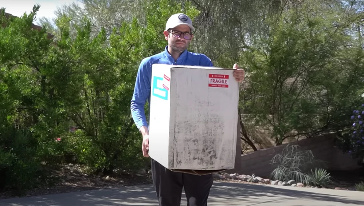 Man holding a large format architectural blueprint or technical drawing outdoors amid trees.