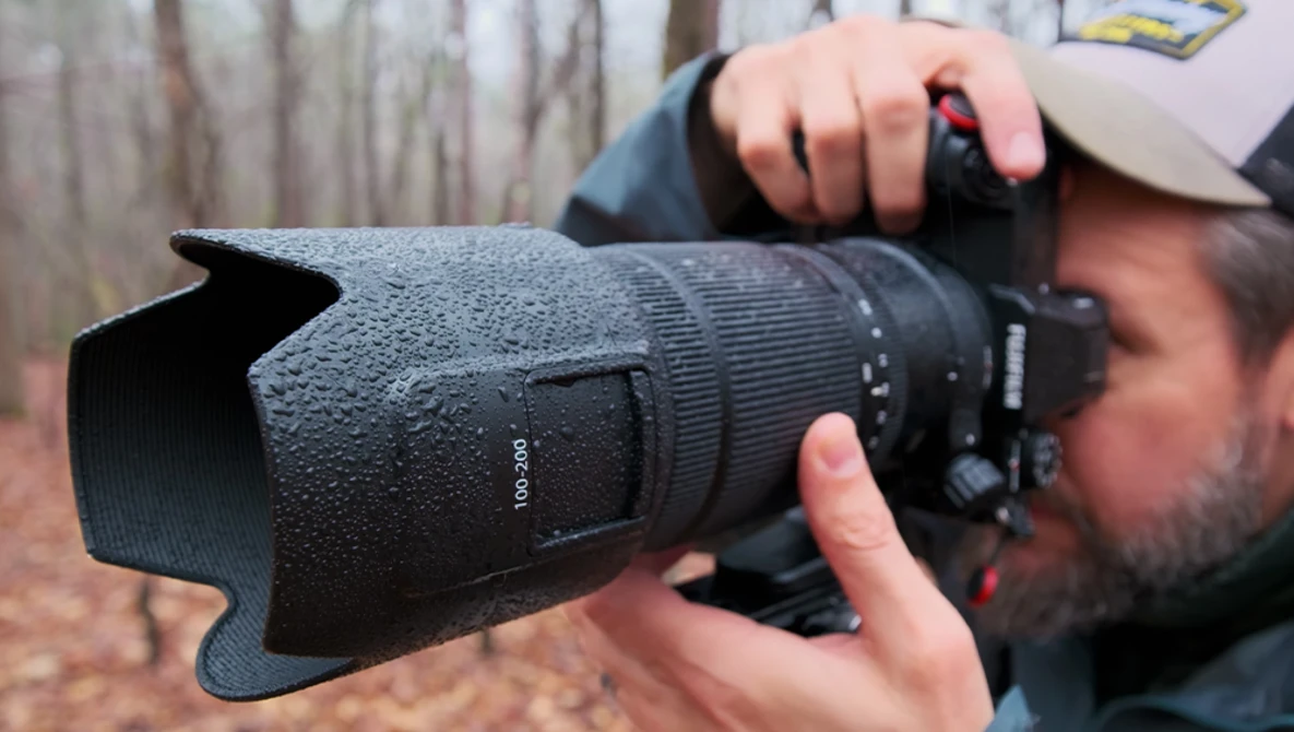 Photographer holding a telephoto lens with lens hood attached, covered in water droplets.