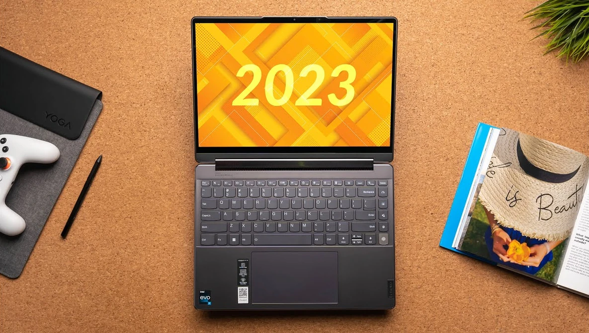 Laptop displaying "2023" on yellow geometric background, surrounded by creative workspace items.