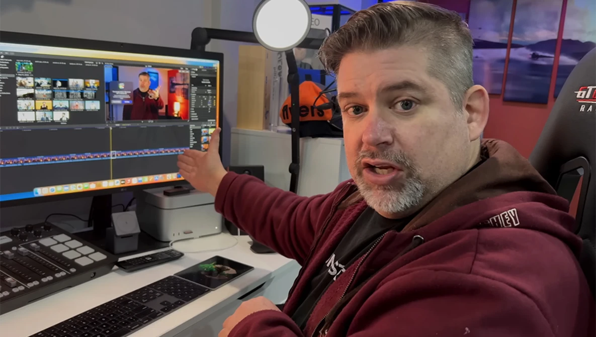 Video editor gesturing at color-graded footage on dual monitors in a studio workspace.