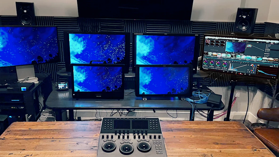 Professional editing workstation with five monitors displaying blue-toned footage and a hardware control panel.