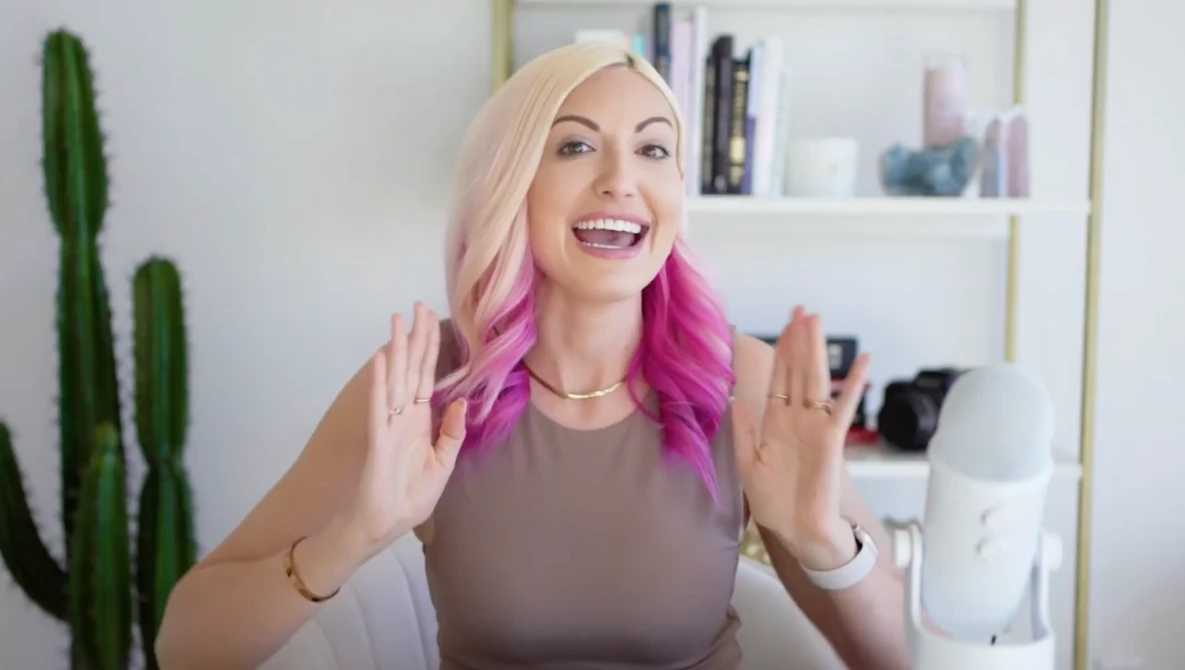 Woman with platinum blonde and magenta ombre hair smiling at camera in home office setting.