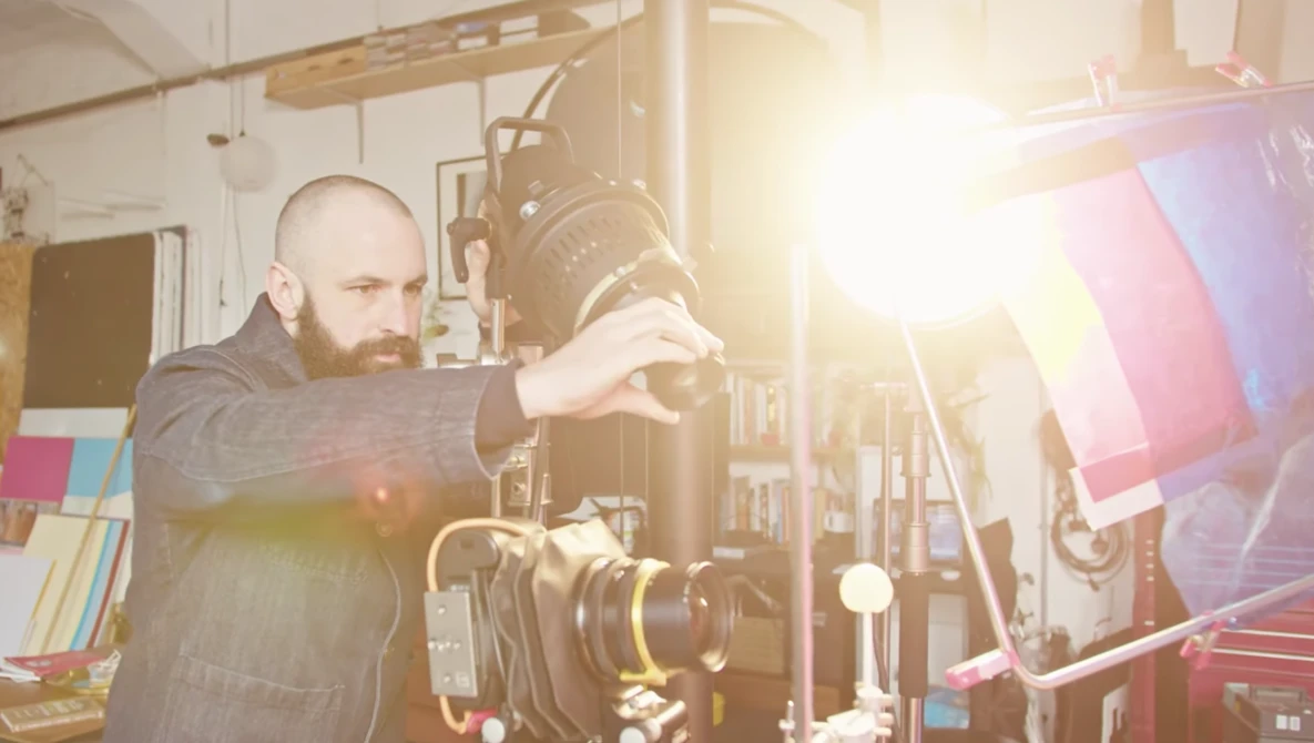 Cinematographer adjusts a large film camera on a studio set with bright lighting equipment.