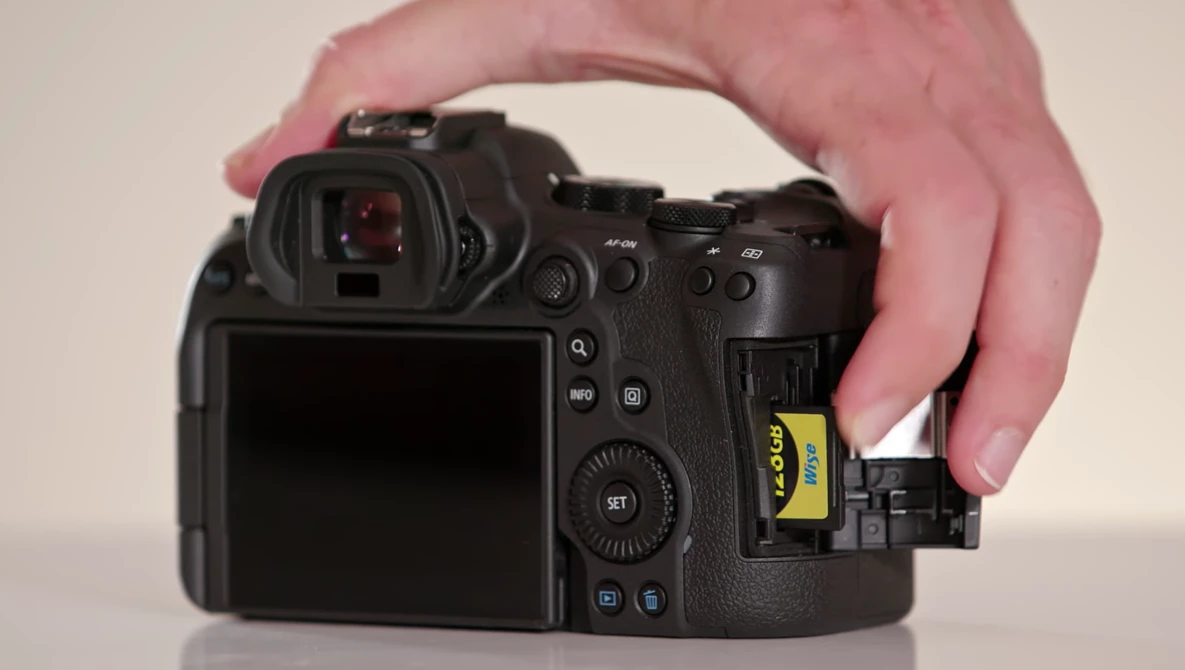 Hand inserting a yellow XQD memory card into the card slot of a professional mirrorless camera.