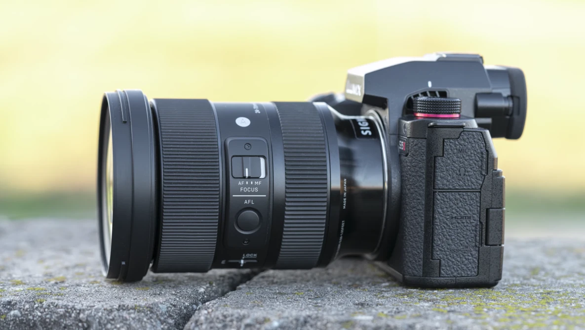 Mirrorless camera with wide-angle zoom lens mounted, positioned on a concrete surface against a blurred yellow-green background.