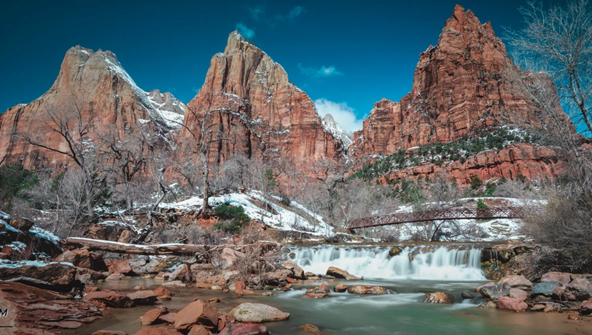 Turquoise river with small waterfall flowing through red rock canyon formations under clear blue sky.