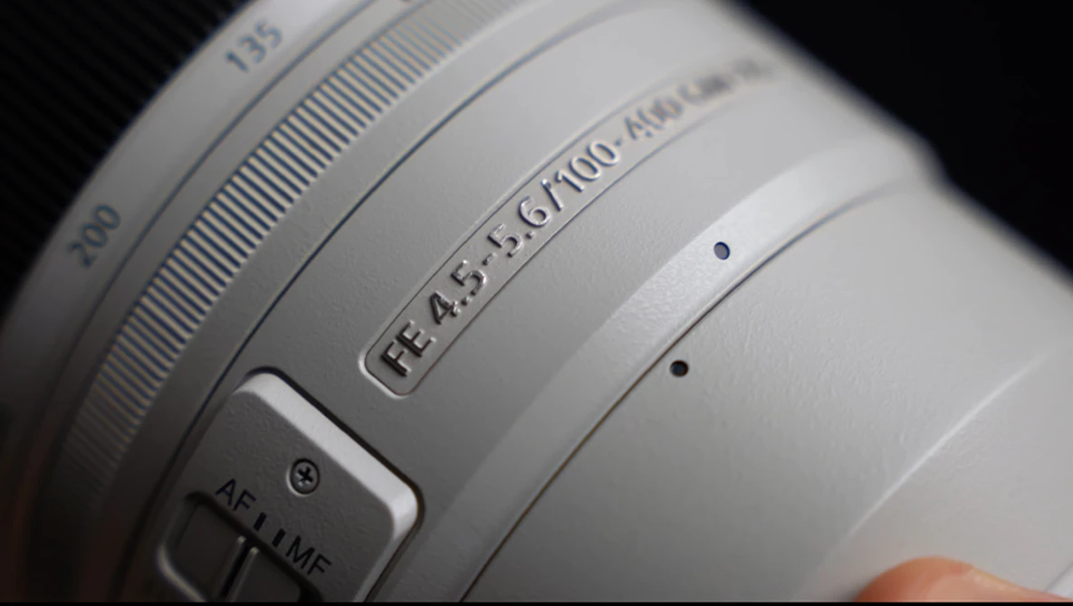Close-up of a white camera lens showing aperture range f/4.5-5.6, focal length 67-100mm, and AF/MF focus mode switch.