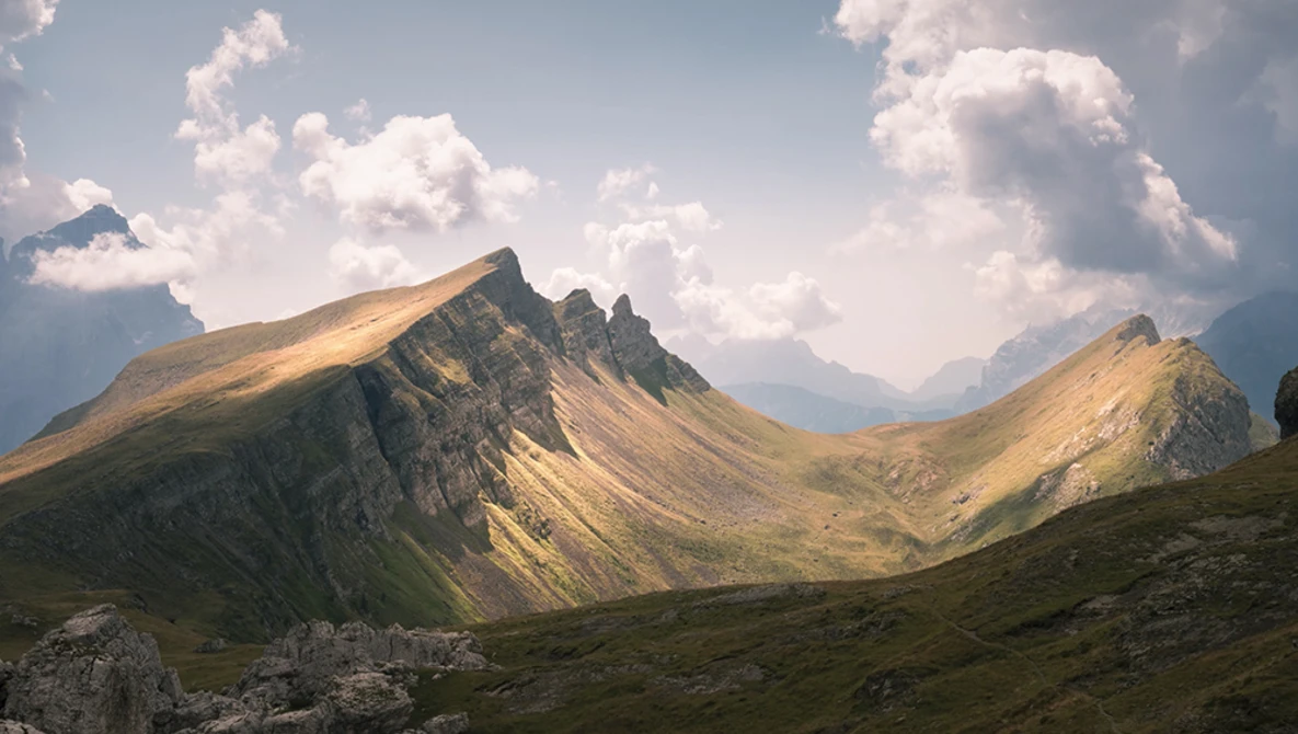 Alpine mountain peaks with golden sunlit slopes under partly cloudy sky.