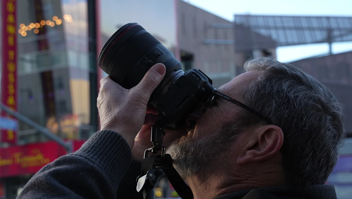 Photographer holding binoculars to his eyes while looking toward an urban skyline during golden hour.