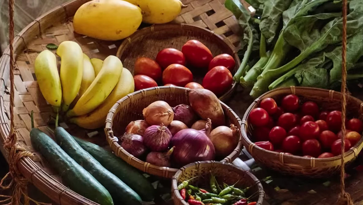 Overhead view of fresh produce arranged in woven baskets, including bananas, potatoes, tomatoes, onions, cucumbers, and green peppers.
