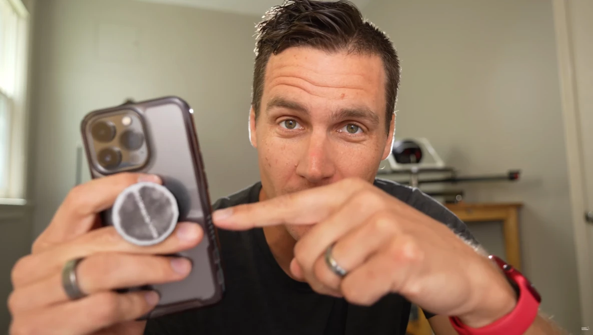 Man holding a smartphone with a magnetic ring attachment, pointing at the device's camera system.