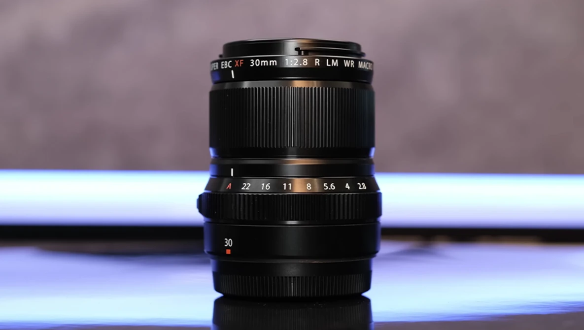 Vintage 30mm camera lens with aperture ring and focus markings displayed vertically against blurred background.