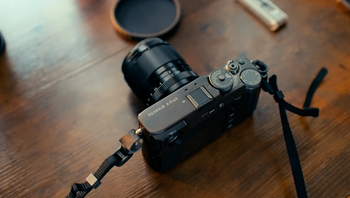 Mirrorless camera with attached lens and shoulder strap on wooden surface.