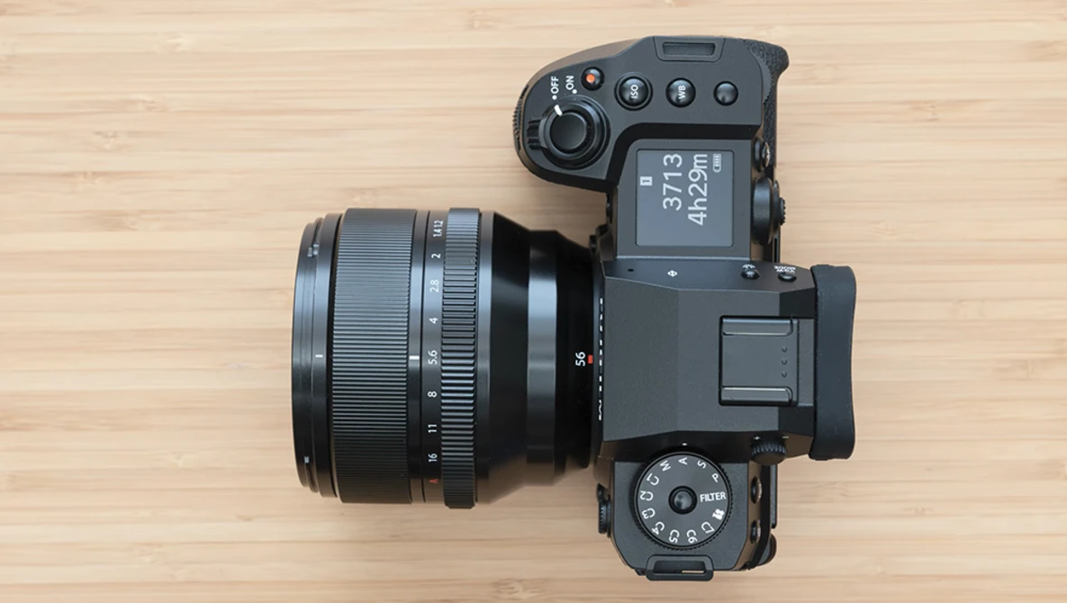 Mirrorless camera with attached prime lens on wooden surface, top-down view.