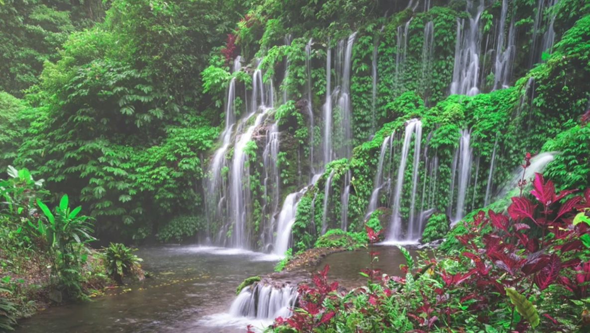 Lush tropical waterfall with multiple cascades flowing into a dark pool, surrounded by dense green foliage and vibrant red flowering plants.
