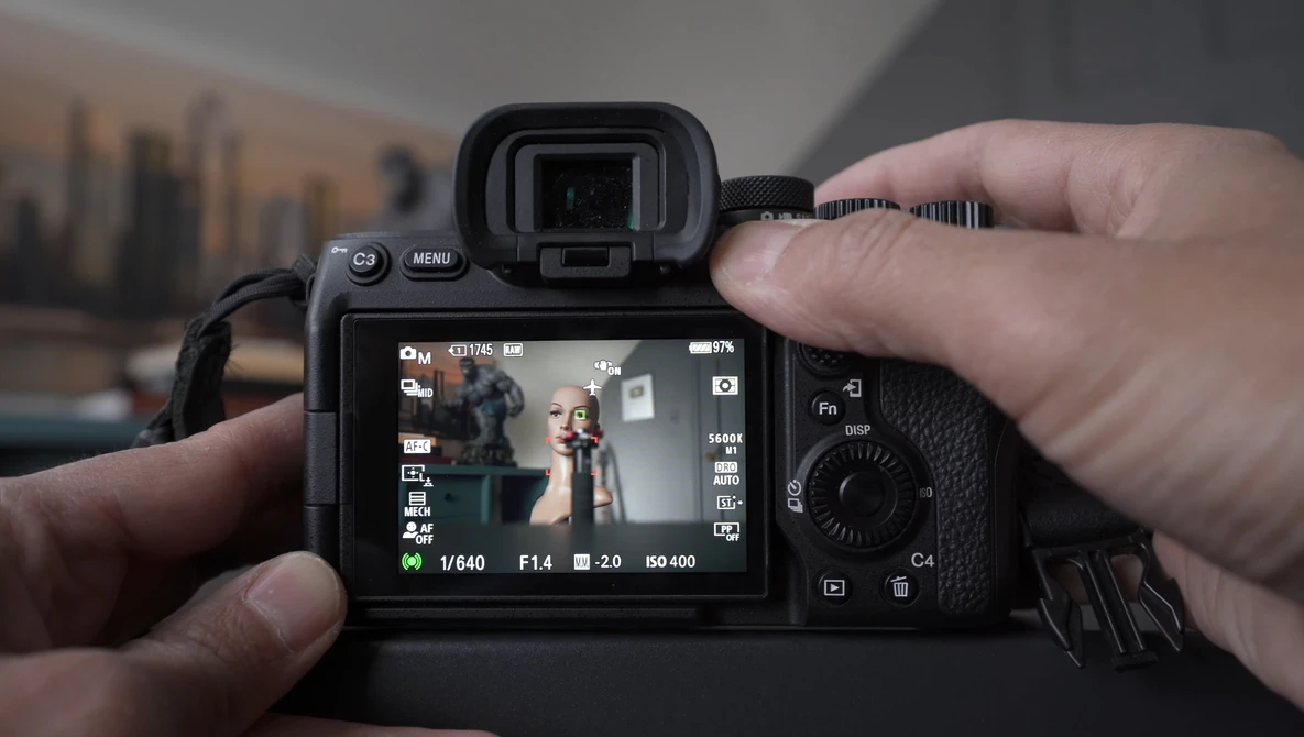 Photographer holding a mirrorless camera with electronic viewfinder extended, displaying live view on rear LCD screen.