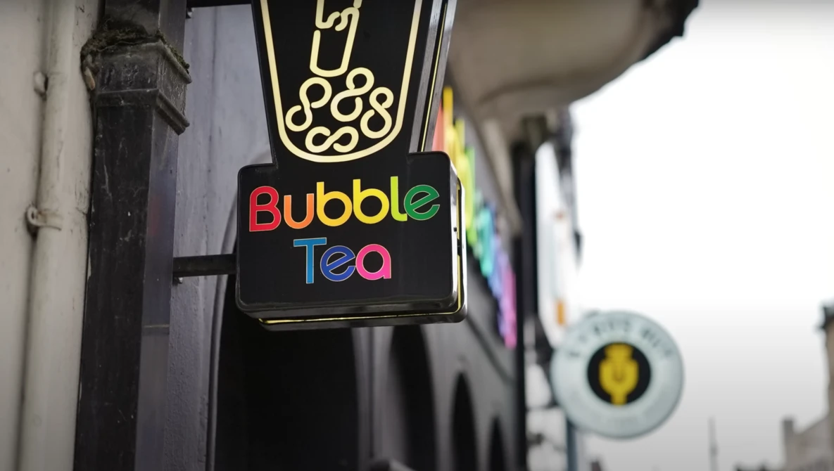 Neon sign for a bubble tea shop with illuminated logo and colorful lettering against storefront.