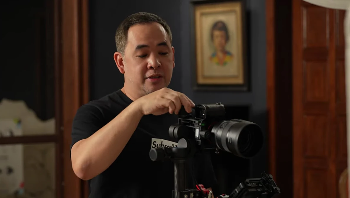 Videographer operating a cinema camera mounted on a tripod in an interior setting.