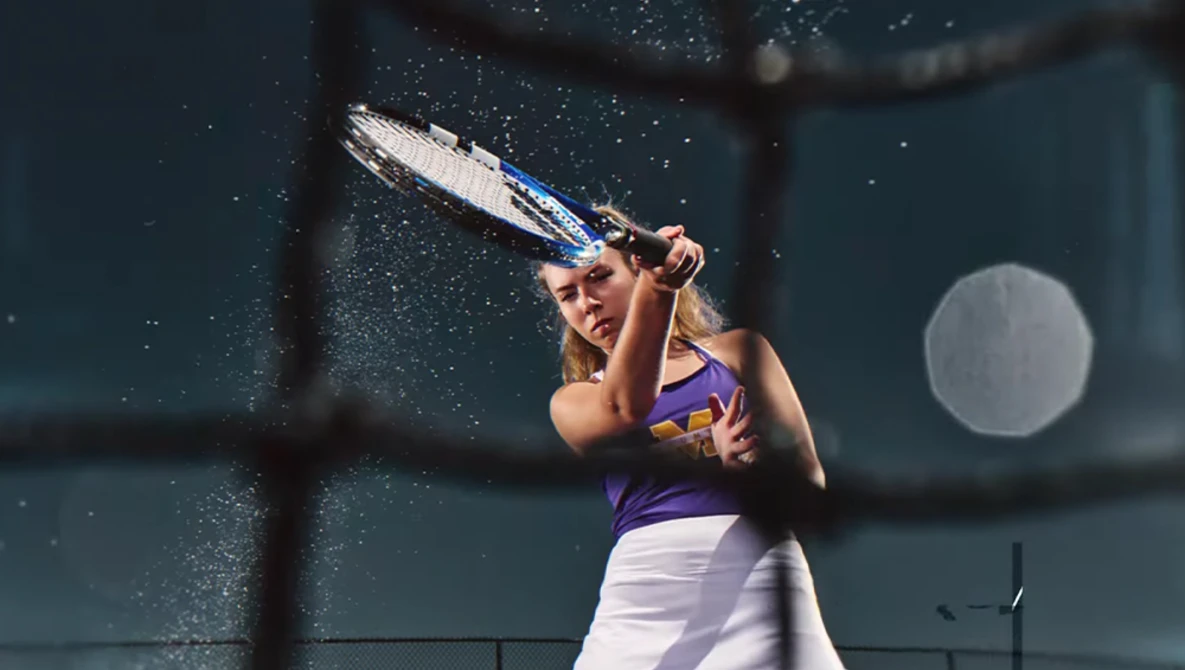 Tennis player mid-swing with water droplets frozen in motion around her racket.