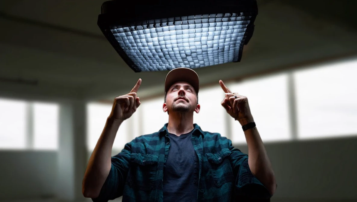 Man in plaid shirt and cap gazes upward at a large grid-pattern ceiling light fixture.