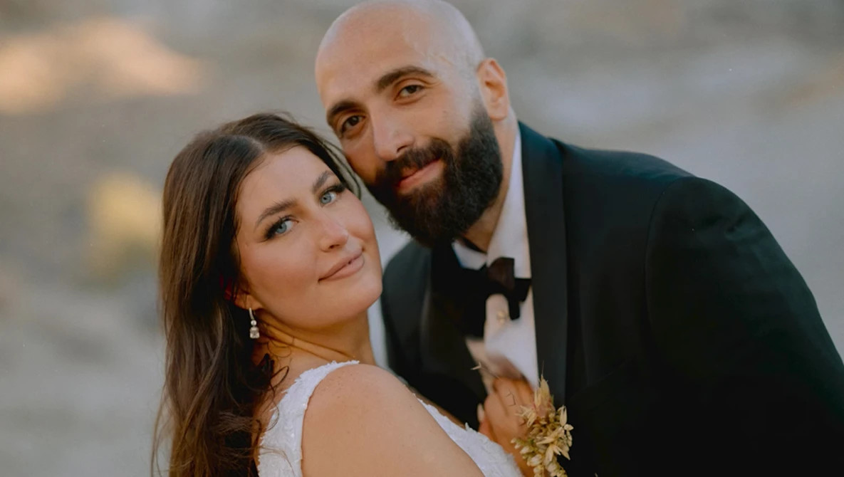 Couple in formal attire posing together outdoors at golden hour.