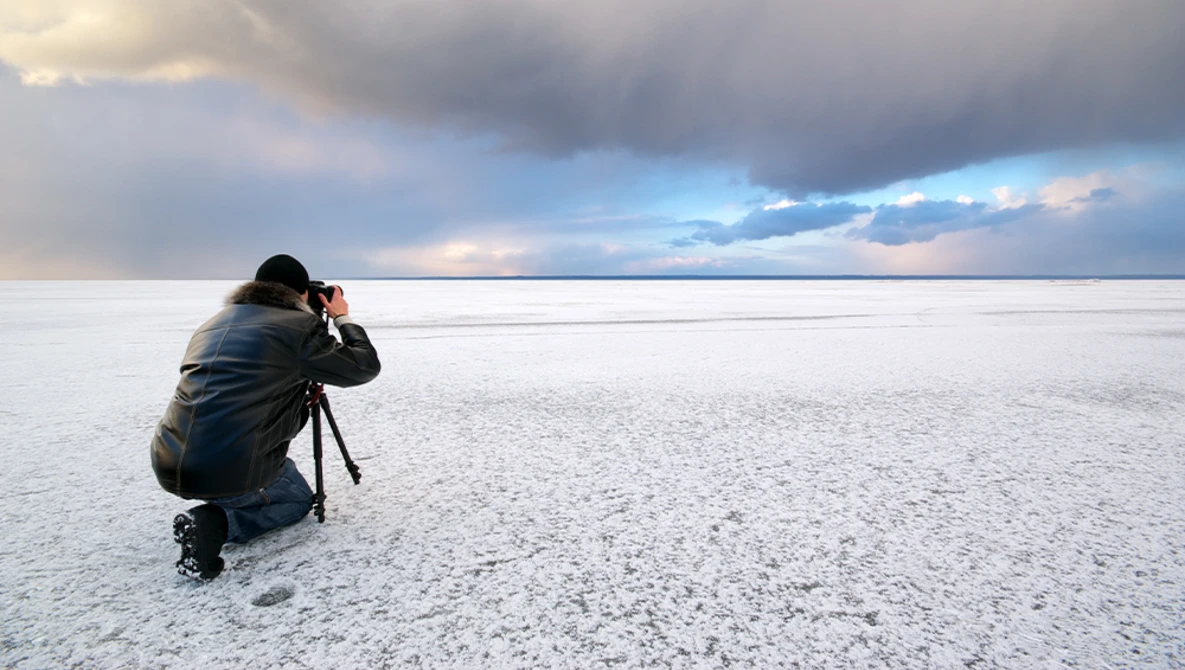 Photographer crouching on a salt flat to capture the dramatic sky reflected in the water.