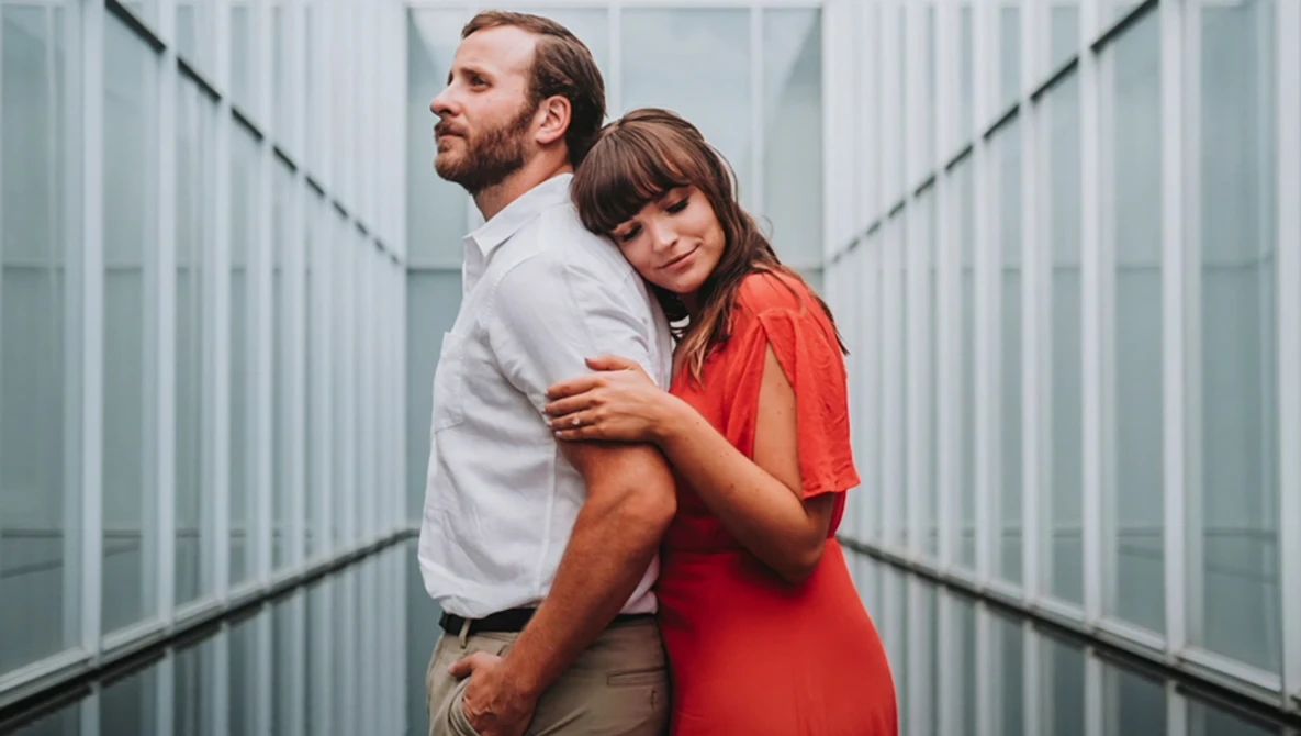 Couple posing together in a modern corridor with symmetrical glass and metal walls.