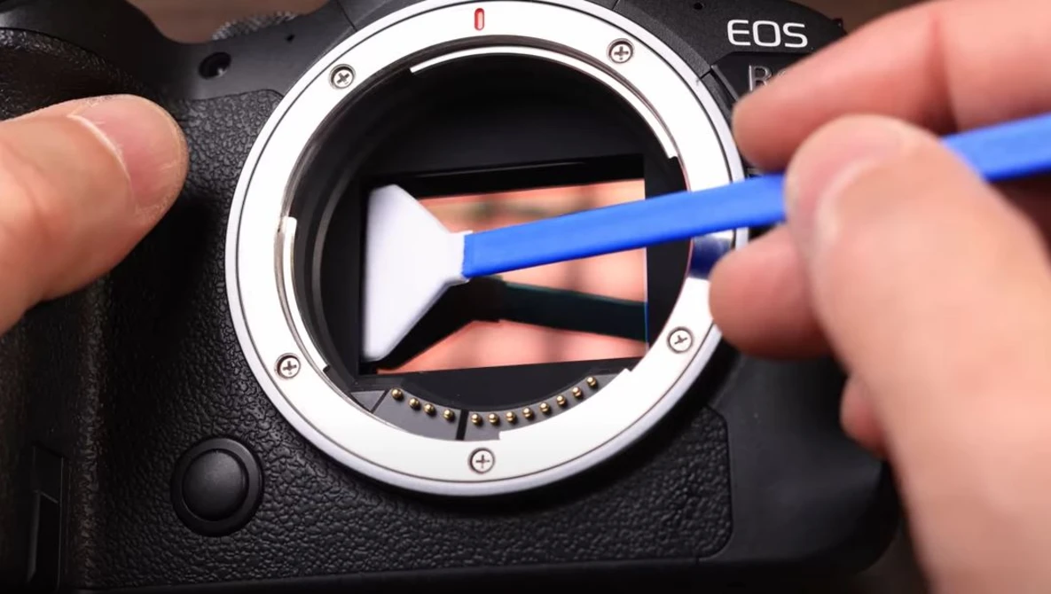 Cleaning the mirror and sensor of a Canon EOS camera with a blue swab and sensor cleaning pen.
