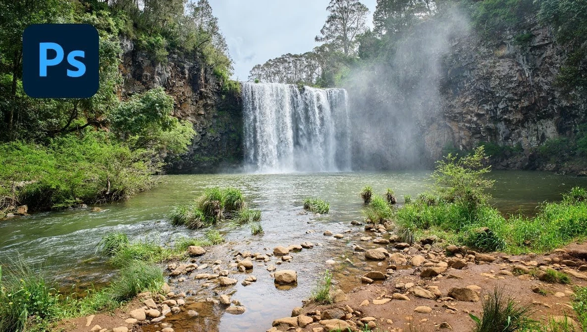 Powerful waterfall cascading into a misty pool surrounded by lush green vegetation and rocky banks.
