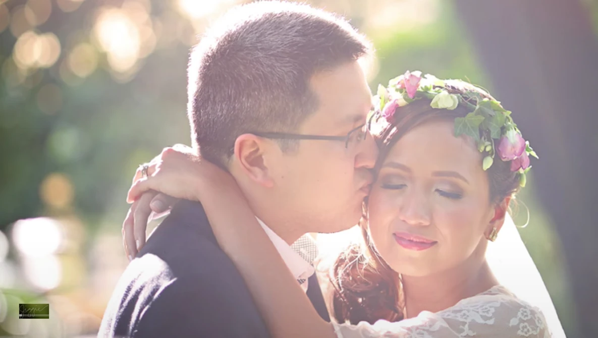 Groom kissing bride's cheek during golden hour, bride wearing flower crown and lace veil.