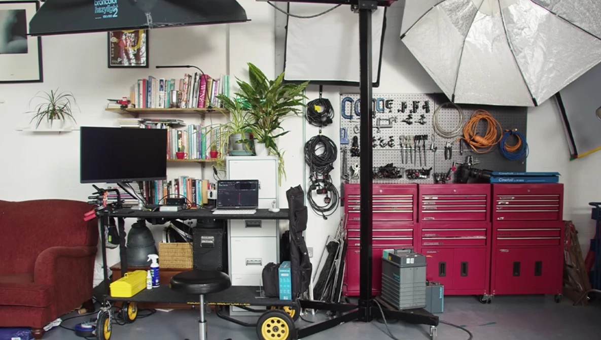 Well-organized photography studio workspace with red tool cabinets, lighting equipment, and shelving along white walls.