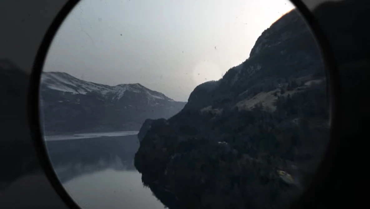 Alpine lake and snow-capped mountains viewed through a circular lens or scope.