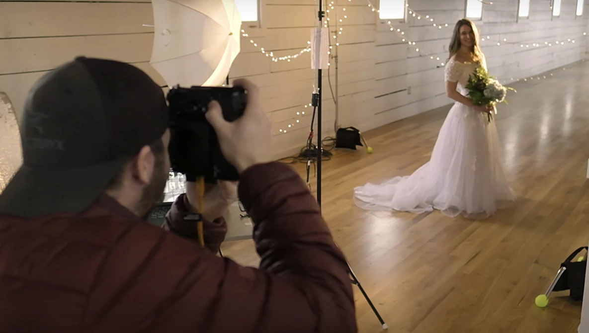 Photographer shooting a bridal portrait of a woman in a white wedding dress holding a bouquet in an indoor venue.