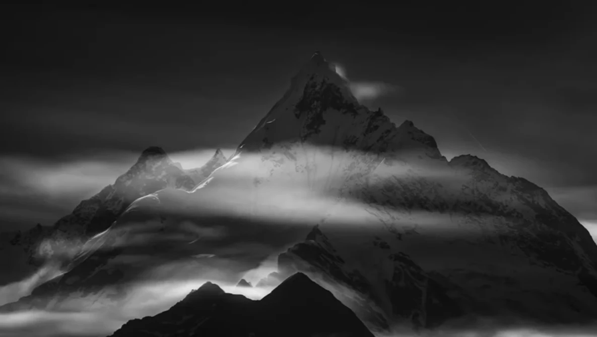 Dramatic black and white mountain landscape with mist swirling around jagged peaks beneath dark clouds.