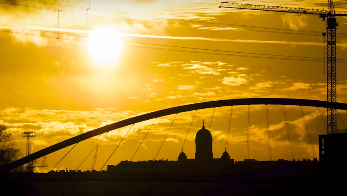 Silhouetted cityscape with arched bridge and cathedral dome against golden sunset sky.