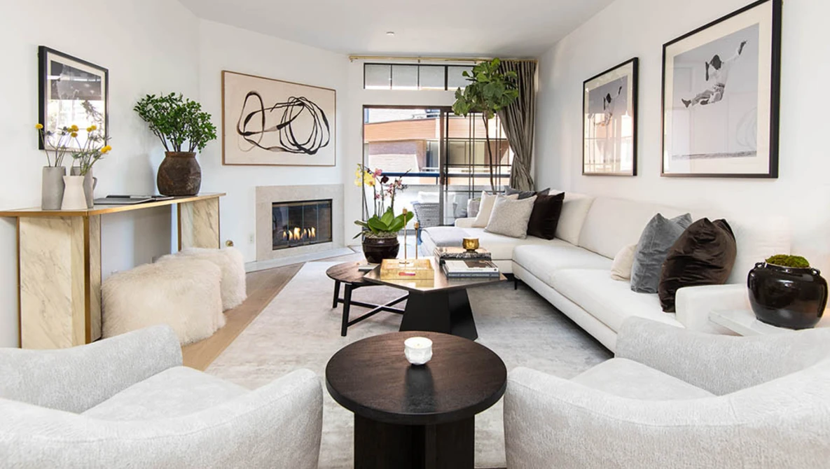 Contemporary living room with neutral furnishings, fireplace, and large windows overlooking urban street.